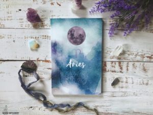 aries journal on a white wood background surrounded by crystals